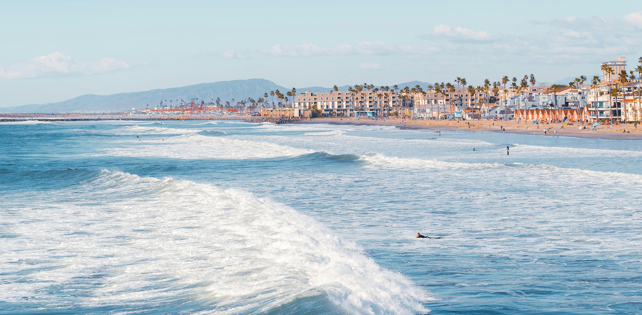 Waves crashing in San Diego in front of palm trees with mountains in the distance